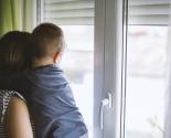 Une mère et son enfant dans les bras regardent par la fenêtre