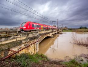 Un train passe sur un pont ferroviaire au-dessus d'un fleuve qui menace de déborder.