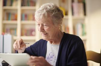 personne âgée assise à une table, en train de naviguer sur une tablette.