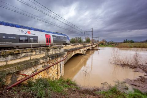 Un train SNCF emprunte un pont au dessus d'une rivière en crue.
