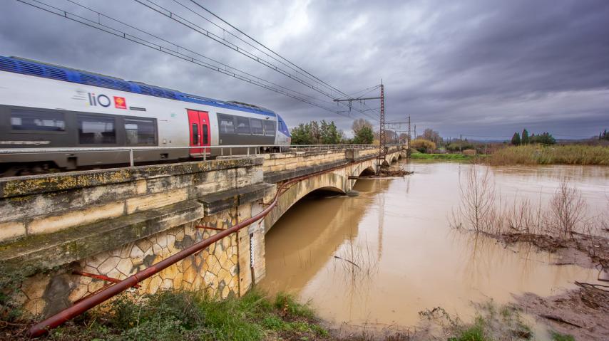 Un train SNCF emprunte un pont au dessus d'une rivière en crue.