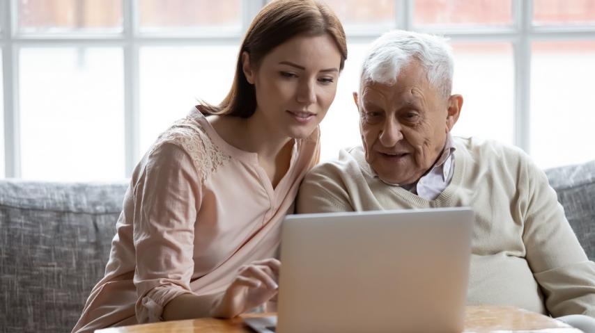 Une jeune femme aide un vieux monsieur à utiliser son ordinateur